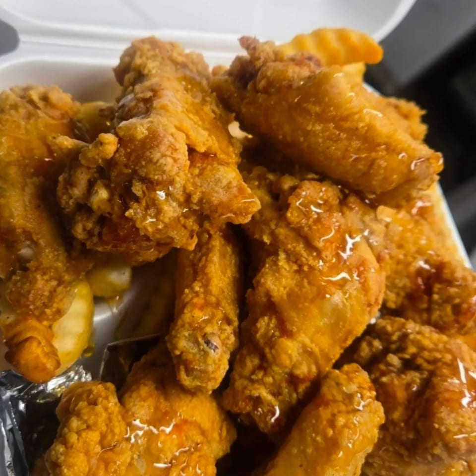 Crispy, golden-brown Cajun chicken wings drizzled with a sweet glaze, served in a white takeout container.
