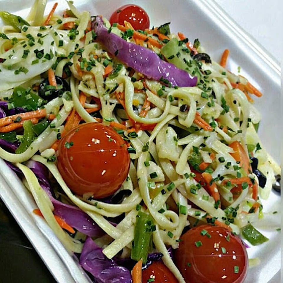Cajun pasta salad with cherry tomatoes, green peppers, carrots, and purple cabbage in a white bowl.