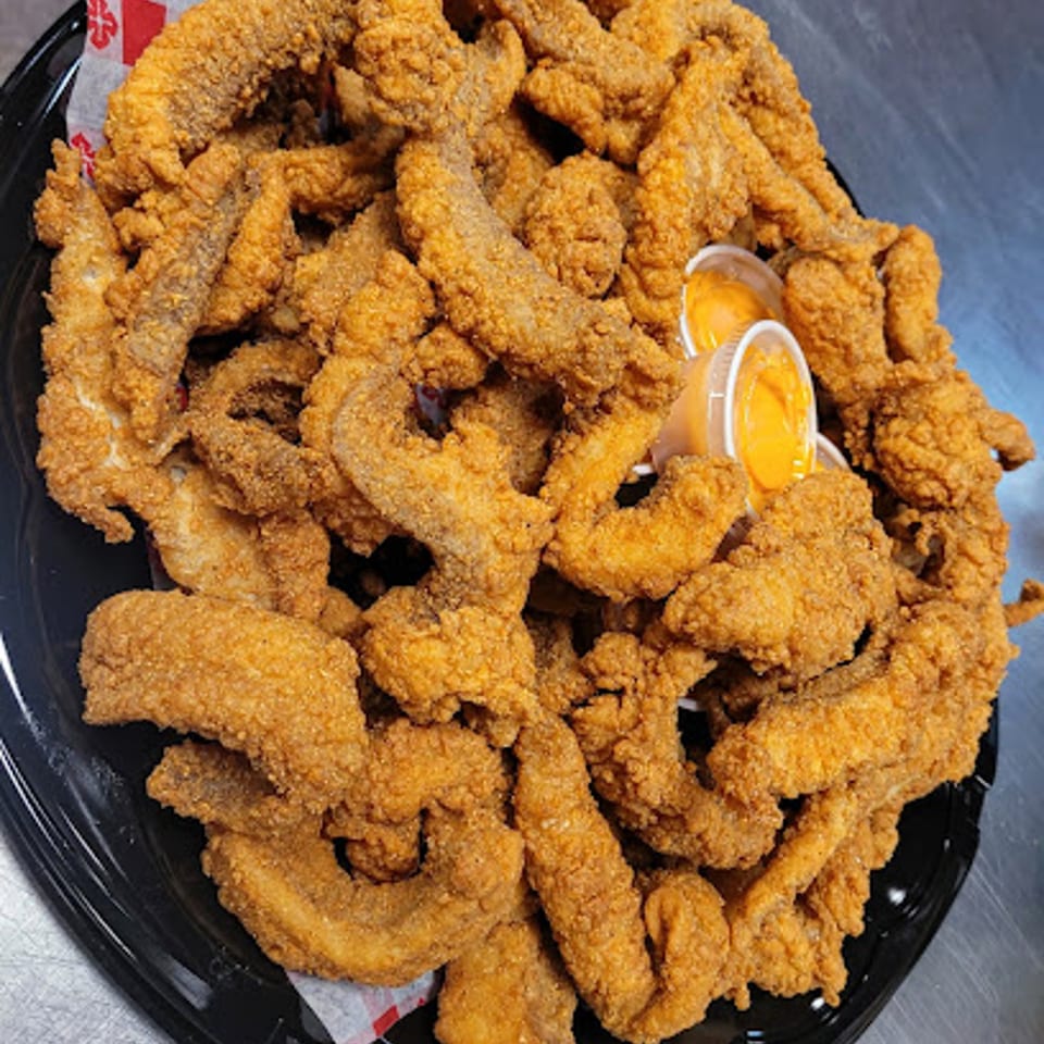 A large platter of golden-brown fried catfish strips with two small cups of dipping sauce.