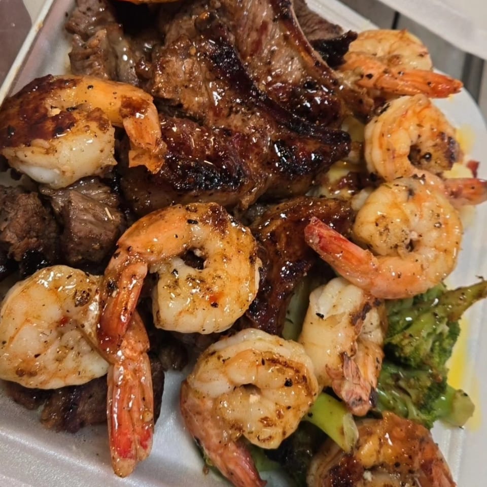 Cajun grilled shrimp and steak with broccoli and rice, served in a white takeout container.