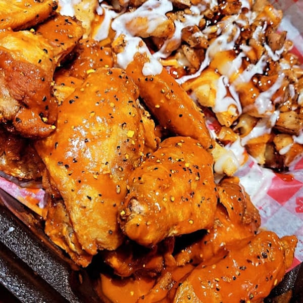 Cajun chicken wings coated in orange sauce with black pepper, alongside seasoned fries drizzled with white sauce.